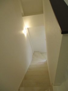 1階から2階への階段：白のアッシュ材の階段に白い壁紙。壁のブラケット照明に反射して美しい。
